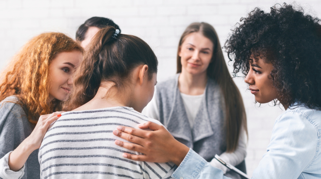 A group photo of five diverse individuals in a circle supporting one another.