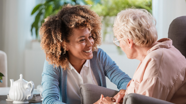 A young female caregiver holding hands with a senior adult. 